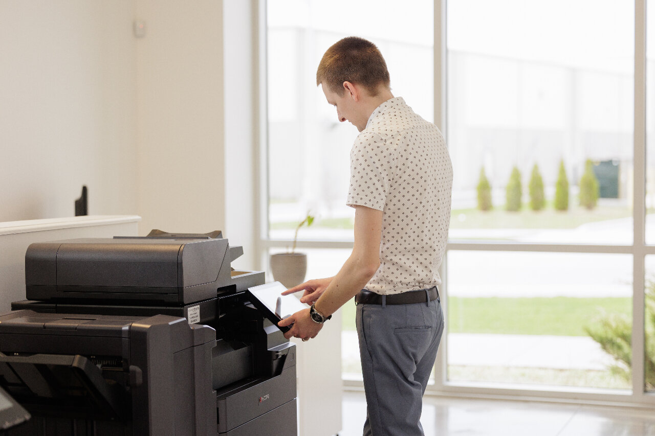 Man standing at Kyocera MFP using touchscreen interface to adjust address book settings